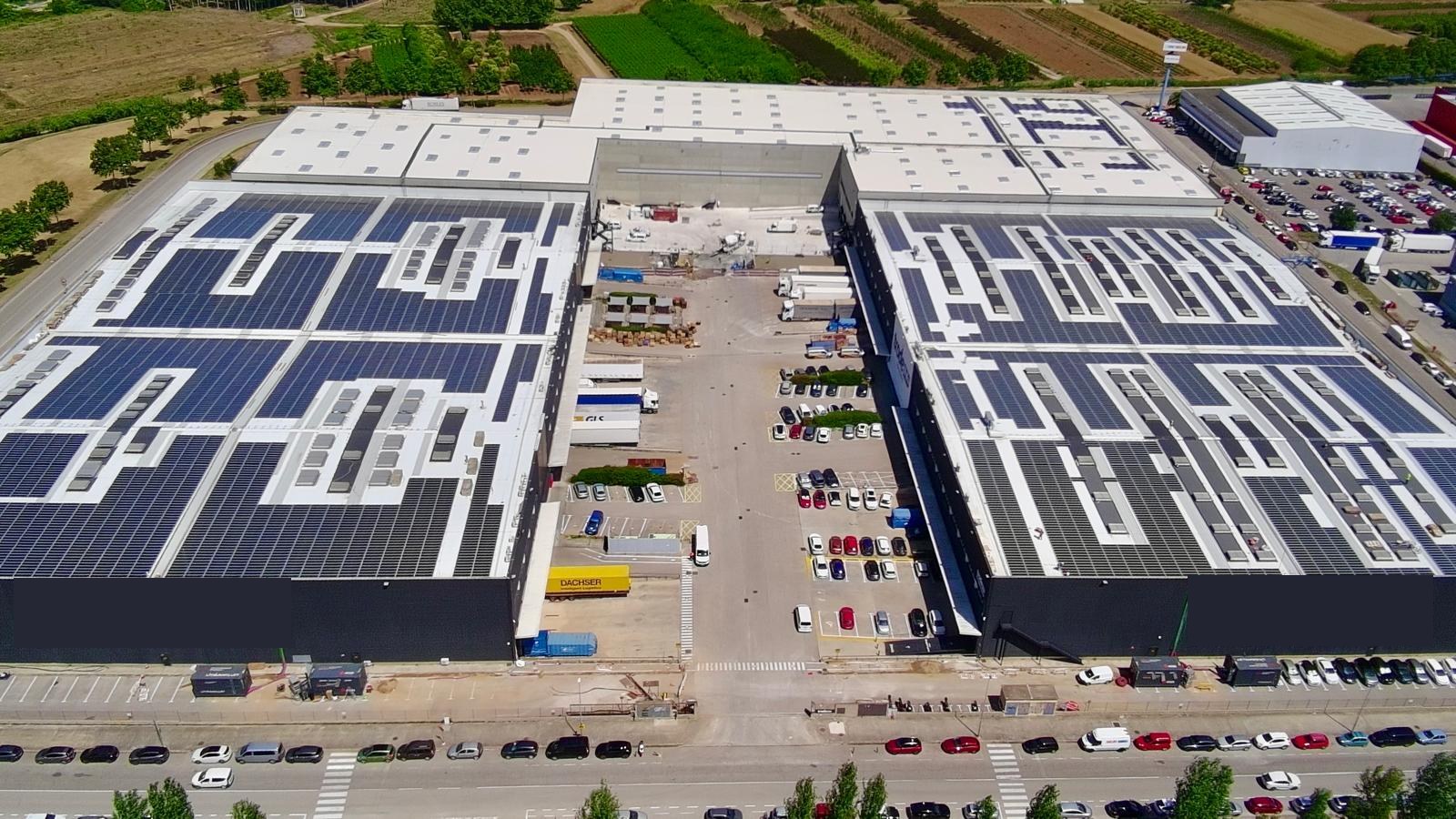 Aerial view of an industrial site with rooftop PV and battery containers in Girona